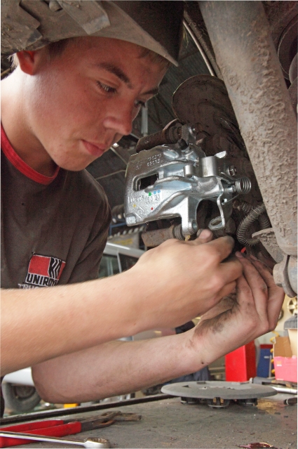 Skilled mechanic fitting new brake calliper at Ian Jones Tyres workshop in Kington, Hereford.