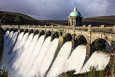 Elan Valley Dam in full flood-flow.  Early winter morning with low sun on dam and grey stormy clouds overhead.